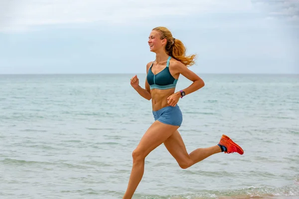Όμορφη αθλητική γυναίκα που τρέχει κατά μήκος την πανέμορφη αμμώδη παραλία, υγιεινό τρόπο ζωής, απολαμβάνοντας δραστήριες καλοκαιρινές διακοπές κοντά στη θάλασσα — Φωτογραφία Αρχείου