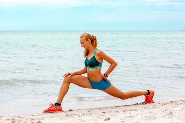 Beautiful sportive woman does stretching along beautiful sandy beach, healthy lifestyle, enjoying active summer vacation near the sea