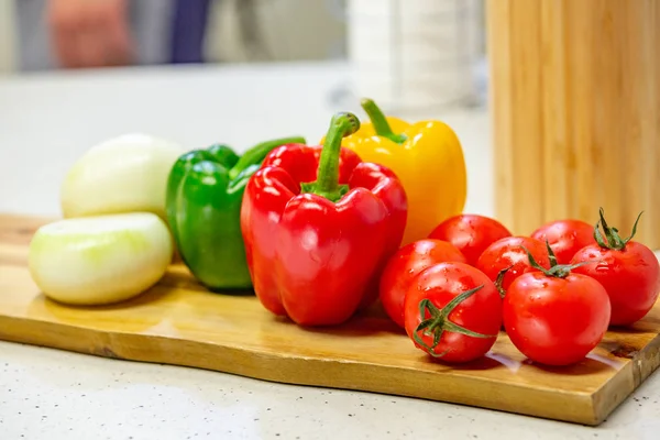 On a wooden Board are vegetables. Tomato, pepper, salad appetizing lie on a wooden Board on a kitchen background