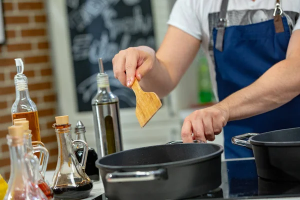 Man cooks meat in a frying pan. Hand using spatula to stir frying pan full of meat. — Stock Photo, Image