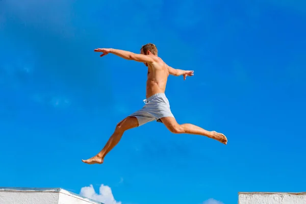 Joven haciendo salto de parkour en el fondo del cielo azul en el soleado día de verano — Foto de Stock