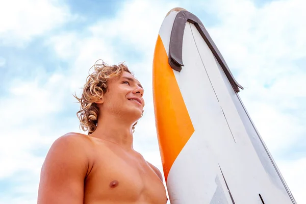 Stattliche Mann zu Fuß mit weißen blanken Surfbrett warten auf Welle zu surfen Spot am Meer Ozeanküste. Konzept von Sport, Fitness, Freiheit, Glück, neues modernes Leben, Hipster. — Stockfoto