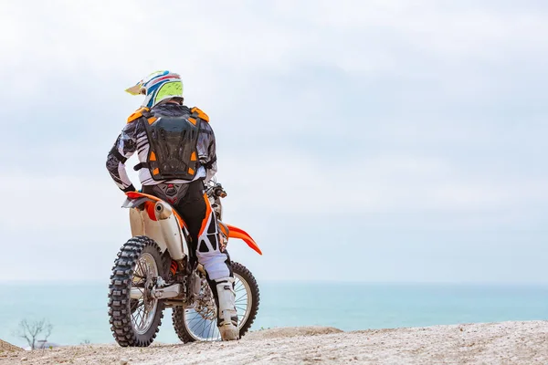 Motociclista in tuta protettiva seduto sulla moto di fronte al mare — Foto Stock