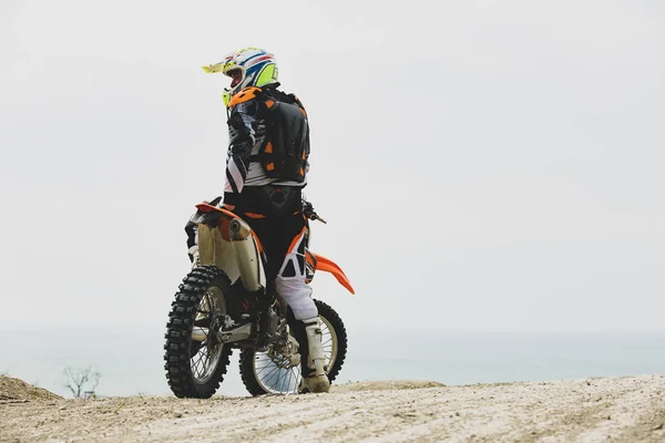Motociclista em um terno protetor sentado em moto em frente ao mar — Fotografia de Stock