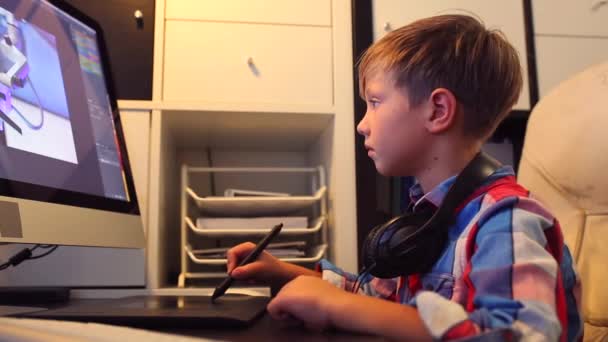 Умный мальчик работает над проектом для своего компьютера. Мальчик работает за компьютером с помощью графического планшета — стоковое видео
