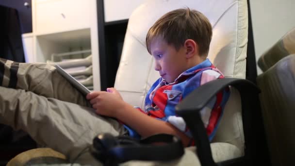 Feliz joven jugando en su tableta sentado en la silla en casa . — Vídeo de stock