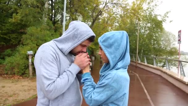 年轻夫妇在户外运动衫在寒冷的天气。男人用呼吸温暖女孩的手. — 图库视频影像