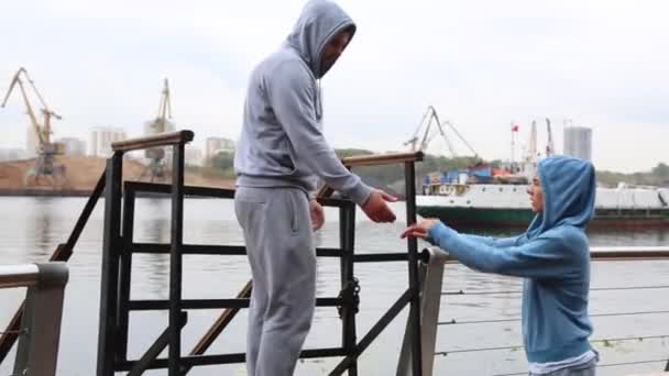 Widok z boku szczęśliwy młody człowiek, obejmując jego dziewczyna piękny cutie. Dorywczo Ogarnięcie para stojący na chodnik city waterfront — Wideo stockowe