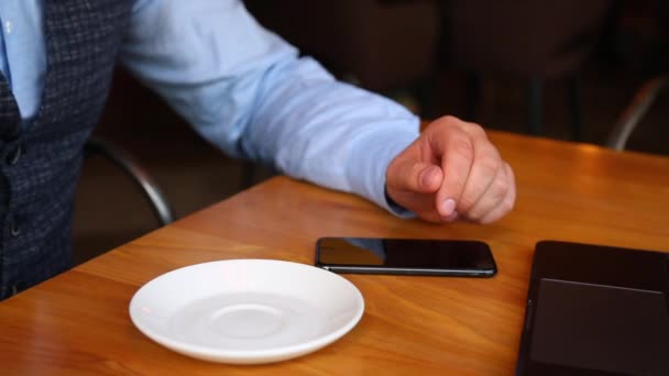 Бізнесмен з ноутбуком в кафе, п'є каву і використовує смартфон . — стокове відео