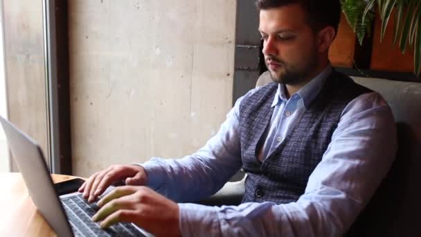 Homem de negócios trabalhando no laptop no café e falando ao telefone . — Vídeo de Stock