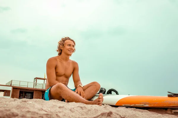 Όμορφος άνδρας κάθεται στην παραλία με λευκό κενό σερφ Διοικητικό Συμβούλιο περιμένει κύμα να σερφάρετε σημείο στο κύμα στον ωκεανό της θάλασσας. Έννοια της άθλημα, fitness, ελευθερία, ευτυχία, νέα σύγχρονη ζωή, hipster. — Φωτογραφία Αρχείου