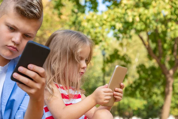 Niños ocupados mirando sus teléfonos mensajes de texto SMS y jugando sentado fuera — Foto de Stock