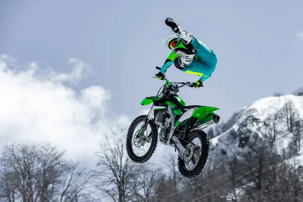 Piloto em uma motocicleta em voo, salta e decola em um trampolim contra as montanhas nevadas — Fotografia de Stock