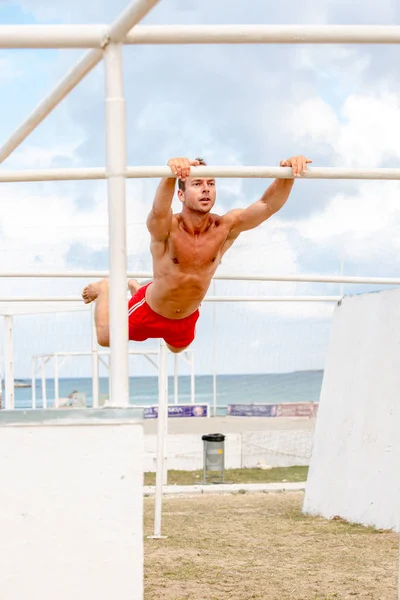 Hombre atlético joven aferrándose a la barra horizontal, al aire libre — Foto de Stock