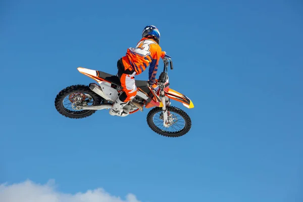 Piloto em uma motocicleta em voo, salta e decola em um trampolim contra o céu azul — Fotografia de Stock