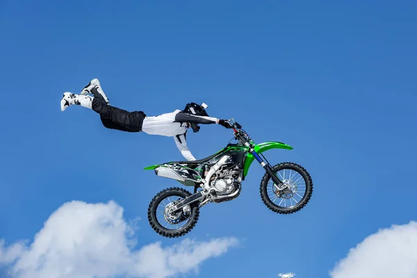 Piloto em uma motocicleta em voo, salta e decola em um trampolim contra o céu azul — Fotografia de Stock