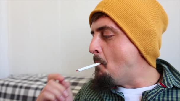 Νεαρός άνδρας, που μοιάζει με ένα hipster, μετά από σκληρή δουλειά καπνίζοντας τσιγάρο με το στοχαστικό πρόσωπο στο μπαλκόνι του — Αρχείο Βίντεο