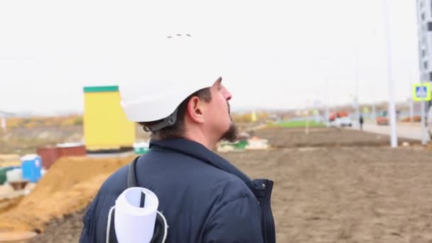 Ingénieur de construction ou architecte en casque avec un plan de construction sur le chantier . — Video