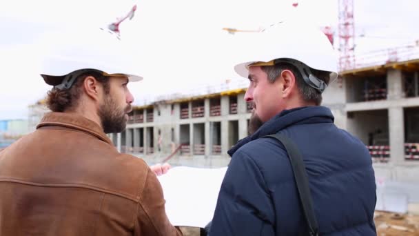 Dos ingenieros hablan del proyecto para el edificio de construcción. Miran ambos proyectos de papel — Vídeos de Stock