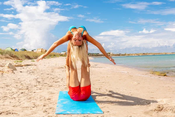 young couple woman and men on the beach doing fitness yoga exercise together. Acroyoga element for strength and balance