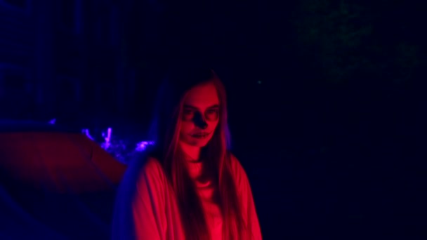 Женщина с мертвым макияжем невесты на Хэллоуин стоит у машины в белом платье невесты в темноте в доме — стоковое видео