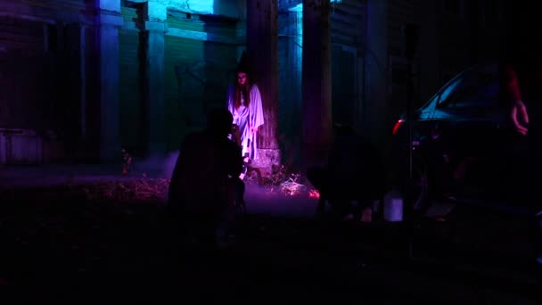 Vrouw met dode bruid make-up voor Halloween staande door de auto in de jurk wit bruid in het donker bij verlaten huis — Stockvideo