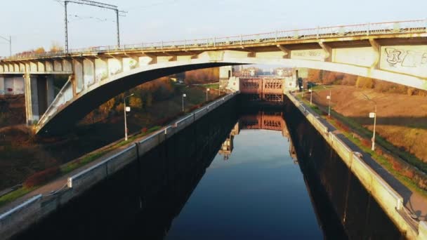 Aerial shot of tall bridge crossing river. Drone flies under the bridge against the autumn landscap — Stock Video