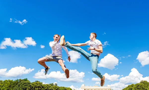 Guys are fighting in the air. Guys are jumping into air and kicking his friend. Guys are fighting in the air against the background of a blue sky