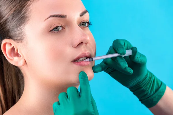 Beautiful woman face and beautician hands with syringe. Doctor makes cosmetic injection in the upper lip. Clean Beauty concept
