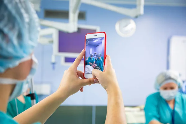 Assistant shooting on the smartphone from the operating room. Medical Team Performing Surgical Operation in Modern Operating Room.