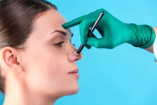 Cosmetic surgeon examining female client in office. Doctor draws lines with a marker, the eyelid before plastic surgery, blepharoplasty. Surgeon or beautician hands touching woman face. Rhinoplasty