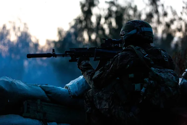 Снайпер озброєний великим калібром, снайперською гвинтівкою, стріляючи по ворожих цілях на відстані від притулку, сидячи в засідці. Вид збоку — стокове фото