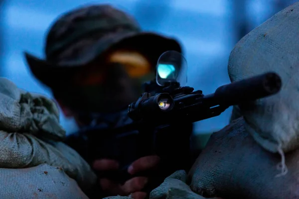 Sniper armé d'un fusil de sniper de gros calibre, tirant sur des cibles ennemies à distance de tir depuis un abri, assis dans une embuscade. Vue de face — Photo