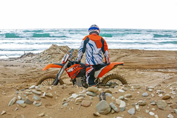 Motocyklista v ochranný oblek sedí na motorce přímo u moře — Stock fotografie