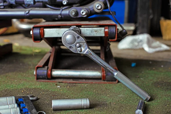 Raden av skruvar och skiftnyckel verktyg på ett golv i verkstad nära reparerade gammal cykel eller motorcykel motor. Industriella scen med utrustning — Stockfoto