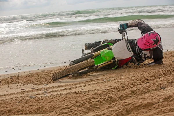 Motorradfahrer stürzte auf einem Motorrad am Strand vor der Kulisse des Meeres — Stockfoto