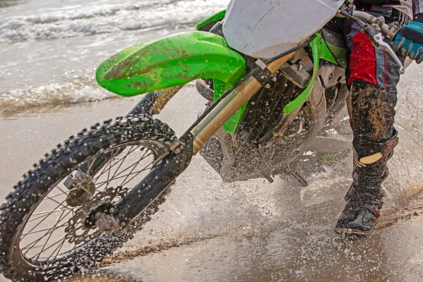 Motociclista en un traje de protección monta una motocicleta en el mar, salpicaduras vuelan desde debajo de las ruedas . — Foto de Stock