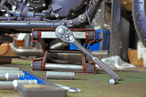 Fila di viti e chiavi utensili su un pavimento in officina vicino riparato vecchio motore moto o moto. Scena industriale con attrezzature — Foto Stock