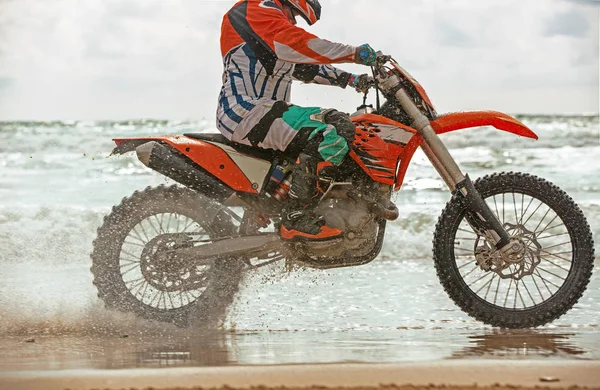 Motorcyklist i en skyddsdräkt rider en motorcykel på havet, stänk flyga från under hjulen. — Stockfoto