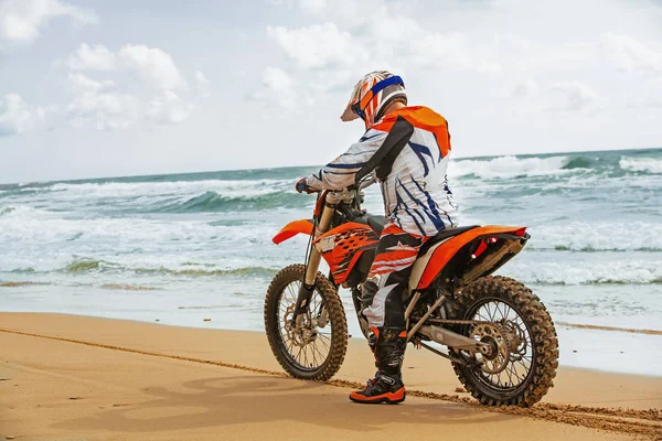 Motociclista in tuta protettiva seduto sulla moto di fronte al mare — Foto Stock