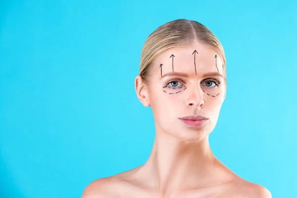 Красивое женское лицо. Красота Портрет молодой женщины, нарисованные линии на лице для косметической операции на синем фоне. Косметический хирург блефаропластика. Подъем — стоковое фото