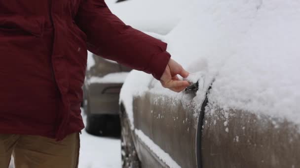 En man rensar snön utanför bilen och öppnar dörren bilen — Stockvideo