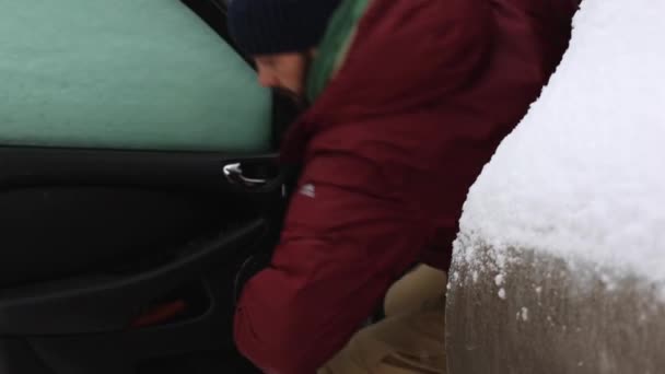 Man is in de auto zitten. Een heleboel sneeuw rond. Man draagt winterjas en cap. — Stockvideo