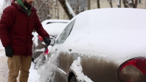 Мужчина чистит снег из машины щеткой в жилом районе — стоковое видео