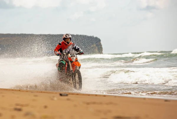 Μοτοσικλετιστής σε ένα προστατευτικό κοστούμι βόλτες μια μοτοσικλέτα πάνω στη θάλασσα, πιτσιλιές πετούν κάτω από τις ρόδες. — Φωτογραφία Αρχείου