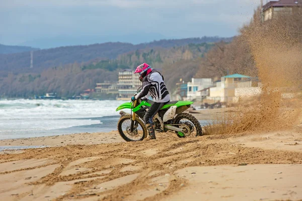 Motorrijder in een beschermend pak een motorfiets rijdt op de zee, spatten vliegen onder de wielen. — Stockfoto