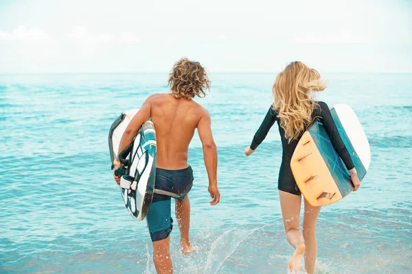 Surfer am Strand - lächelndes Surferpaar, das am Strand spazieren geht und im Sommer Spaß hat. Extremsport und Urlaubskonzept — Stockfoto