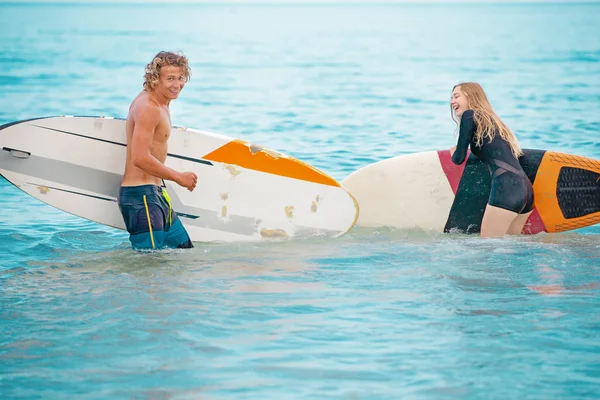 Σέρφερ σε την παραλία-χαμογελώντας ζευγάρι των surfers περπάτημα στην παραλία και έχοντας διασκέδαση το καλοκαίρι. Ακραία έννοια άθλημα και διακοπές — Φωτογραφία Αρχείου