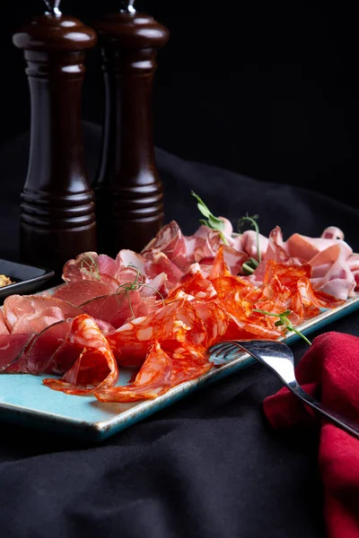 assorted cold meat, prosciutto, slices ham, beef jerky, salami, meat and mustard on black background. Meat appetizer, catering food concept.