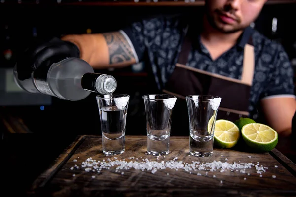 Barman derramando espírito duro em pequenos copos, como doses alcoólicas de tequila ou bebida forte — Fotografia de Stock